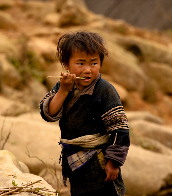 Black Hmong boy chewing on bamboo